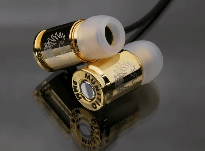 A pair of gold Munitio NINES earphones shaped like 9mm cartridge casings, with white silicone ear tips and a black cable, the base of one housing stamped MUNITIO 9MM around the rim